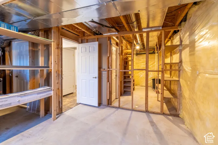 Unfinished storage area featuring exposed wood framing, concrete flooring, built-in shelving, and vapor-barrier insulation