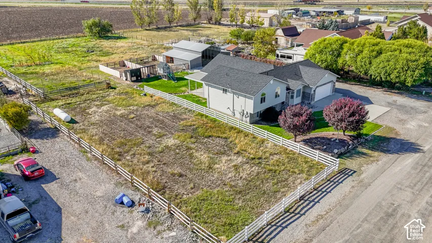 Aerial perspective of a multi-structure property featuring a detached garage, white rail fencing, a covered patio, and mature landscaping