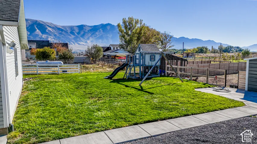Backyard featuring a manicured lawn, concrete patio, perimeter fencing, and prominent mountain backdrop