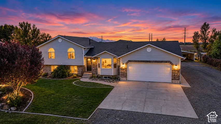 Split-level exterior featuring light horizontal siding, stone veneer accents, an attached two-car garage, arched windows, and a paved concrete driveway