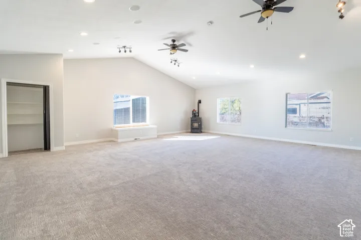 Expansive room featuring vaulted ceilings, neutral wall-to-wall carpeting, multiple ceiling fans, recessed lighting, and a cast-iron stove