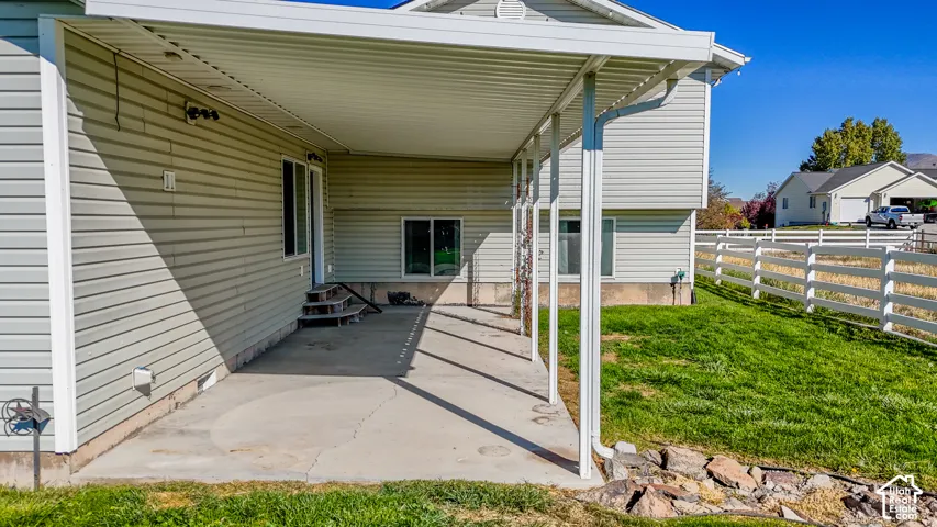 Covered concrete patio with metal support columns, vinyl siding exterior, and white ranch-style fencing