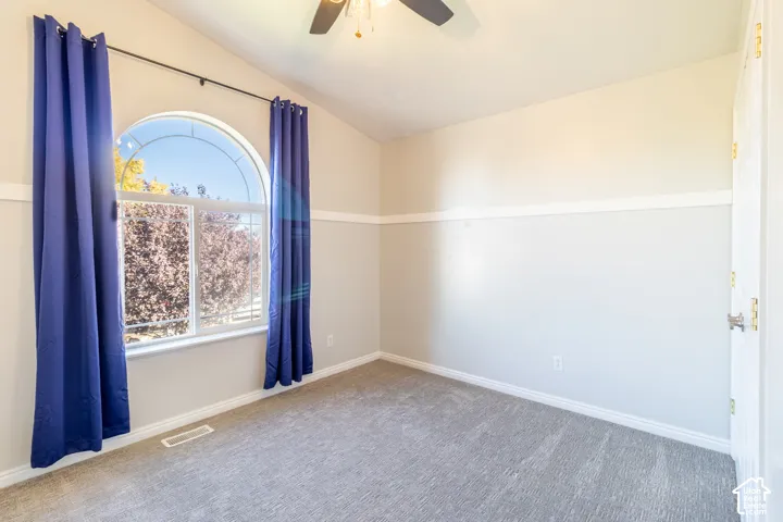 Room featuring vaulted ceilings, an arched window, chair rail molding, and neutral carpeting