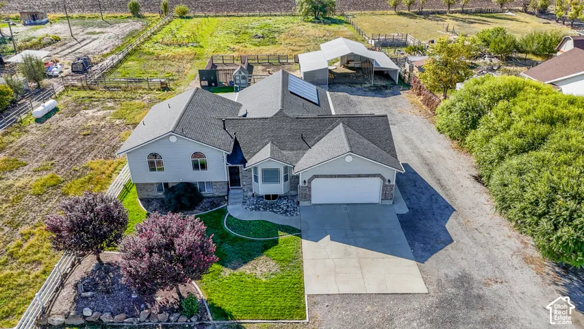 Single-level residence featuring a multi-gabled asphalt shingle roof with integrated solar panels, an attached two-car garage, concrete driveway, and expansive acreage including a detached metal-frame covered structure