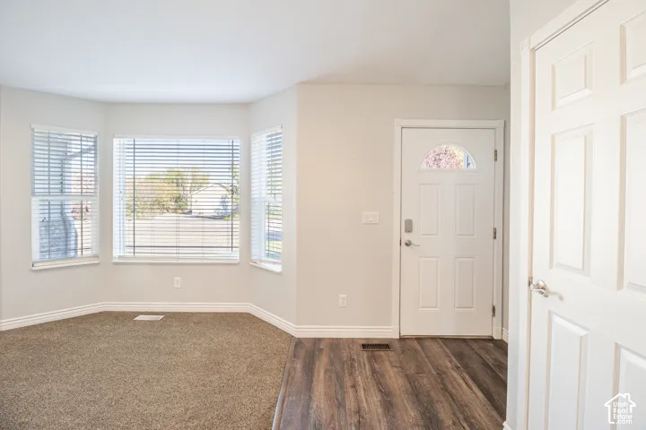 Interior space featuring a bay window, wood-finish flooring, wall-to-wall carpeting, and a white entry door with a half-moon light insert