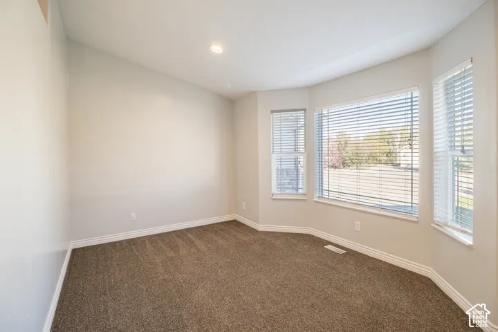Neutral-toned interior space featuring wall-to-wall carpeting, recessed ceiling lighting, and a multi-panel bay window configuration