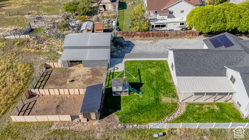 Aerial property perspective featuring a fenced corral, detached storage structure with a metal roof, solar panel array, and a covered patio