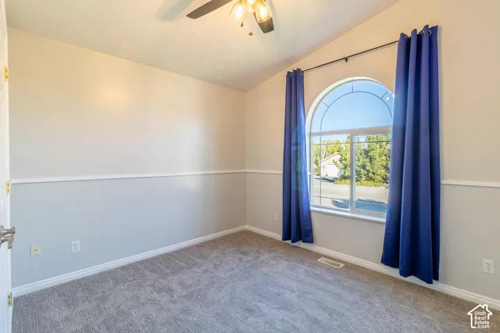 Vaulted ceiling with a central light fixture, arched window, two-tone wall paint, chair rail molding, and carpeting