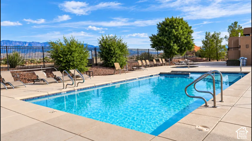 In-ground swimming pool featuring a concrete surround, metal perimeter fencing, and mountain scenery