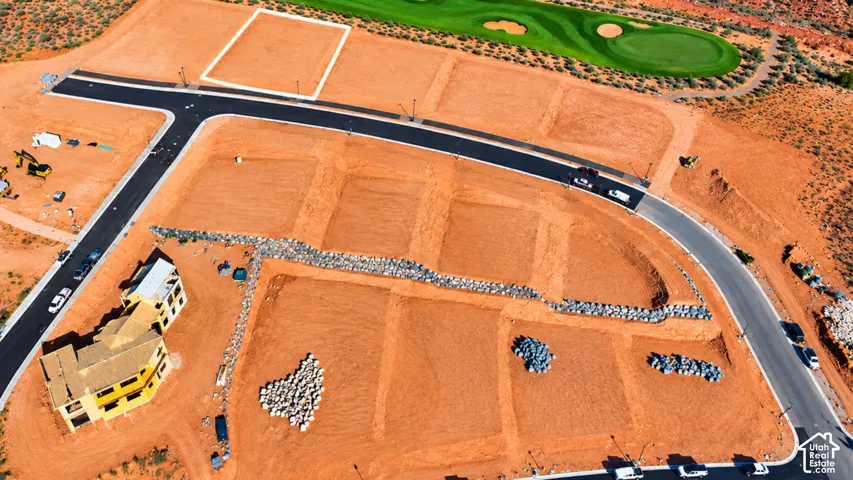 Aerial perspective of residential land parcels featuring paved asphalt roads, natural terrain, stacked stone retaining walls, and proximity to a golf course