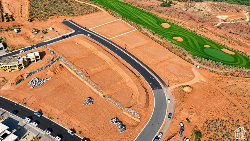 Elevated residential land parcel featuring paved street access, graded building pad, stone retaining walls, and proximity to an adjacent golf course