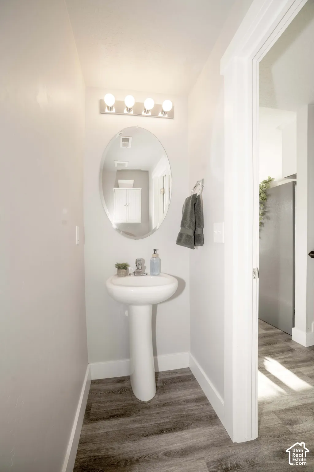 Pedestal sink with chrome faucet, oval wall-mounted mirror, four-light vanity fixture, and LVP flooring