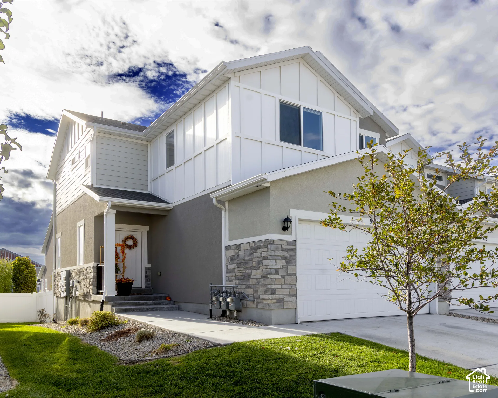 Two-story exterior featuring a mix of horizontal siding, vertical board-and-batten siding, and stone veneer accents, complete with a concrete driveway and attached garage