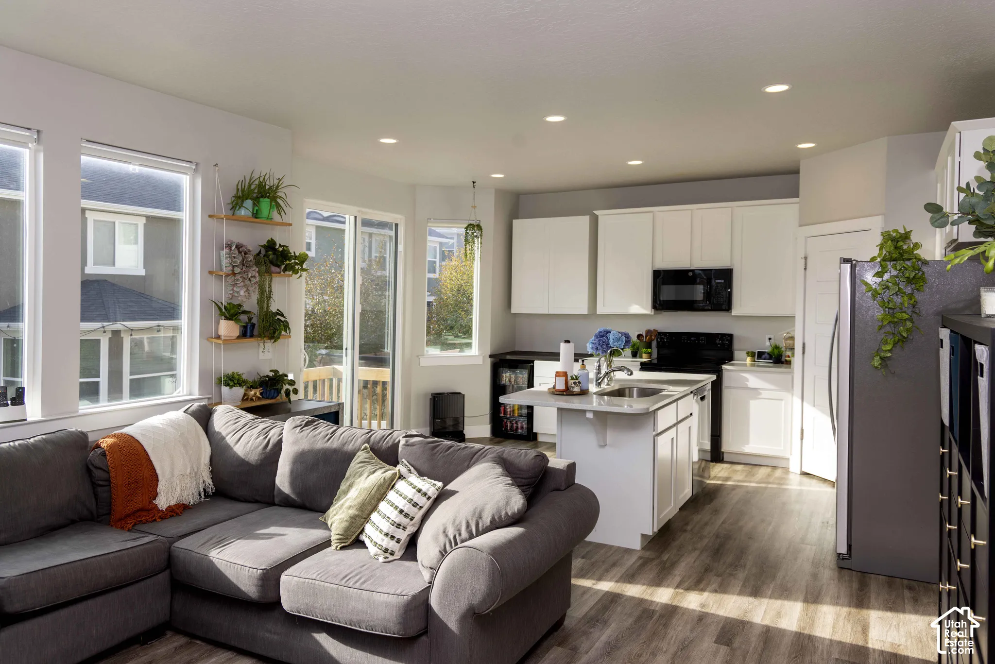 Open-concept interior featuring LVP flooring, white cabinetry, a kitchen island with a built-in sink, recessed lighting, and large windows with sliding glass door access