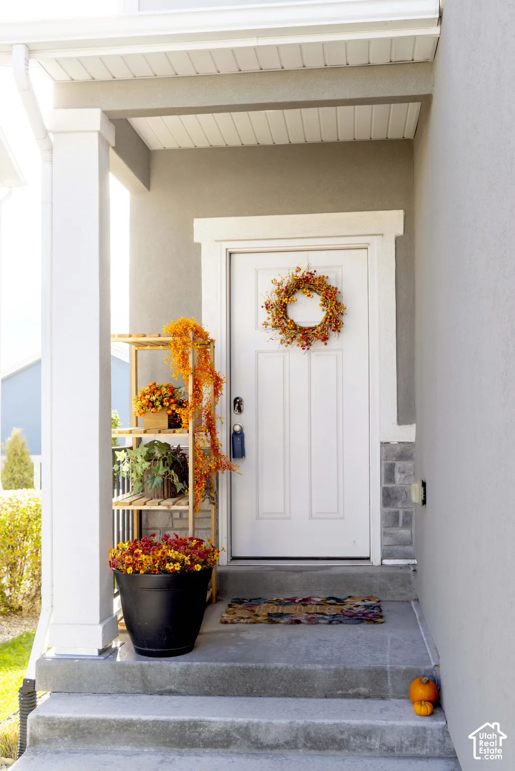 Covered porch featuring a painted four-panel door, concrete porch steps, and stone veneer accents