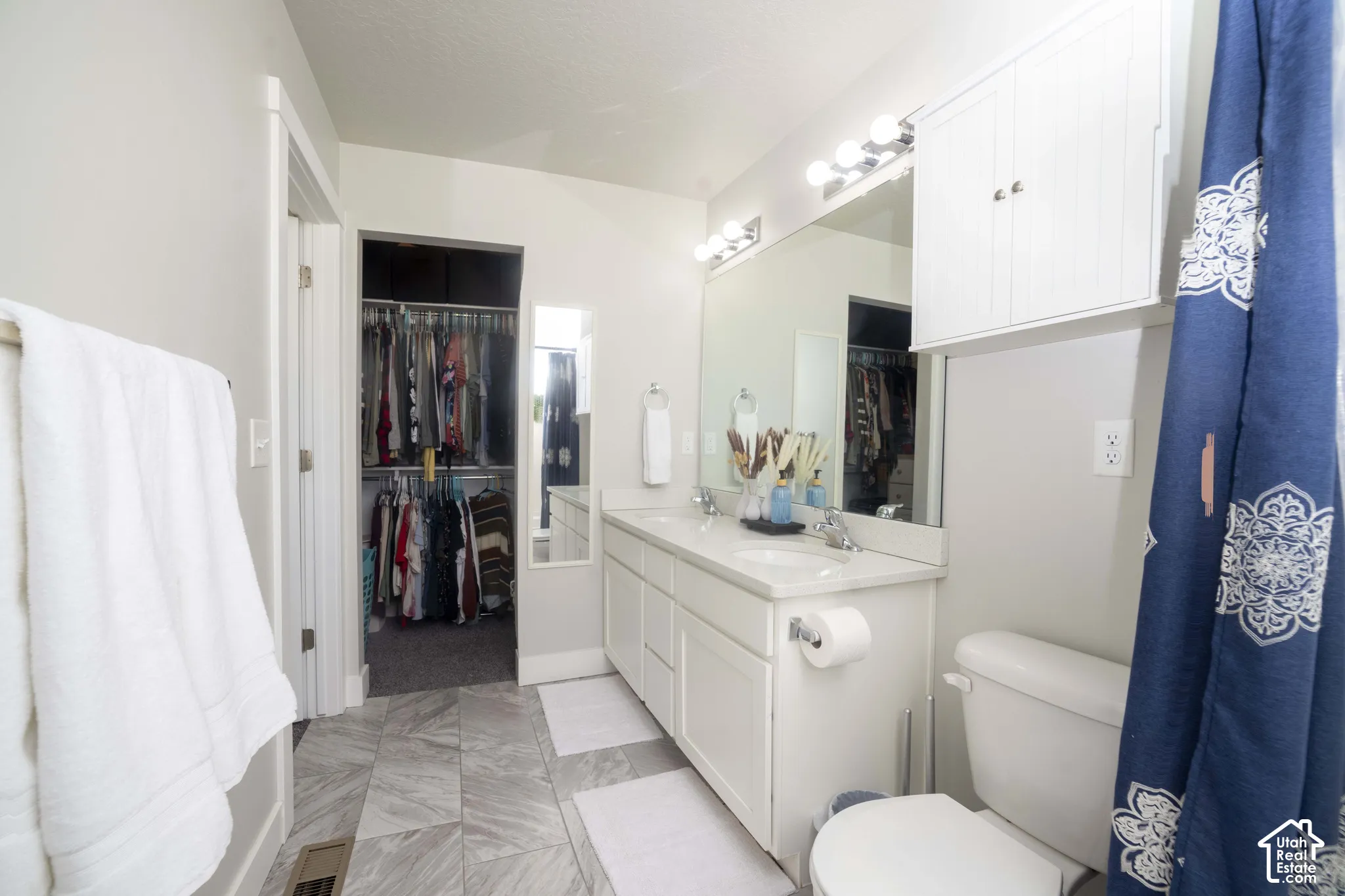 Dual-sink vanity with solid-surface countertop, full-width vanity mirror, built-in wall cabinetry, and stone-patterned tile flooring