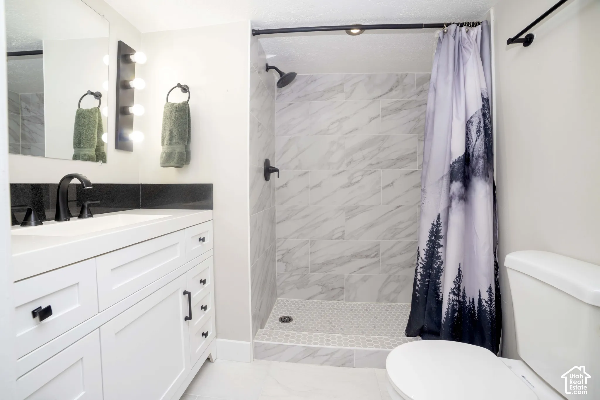 Bathroom featuring a white vanity cabinet with black hardware, dark countertop, walk-in shower with large-format wall tile and hexagonal floor tile, and matte black plumbing fixtures
