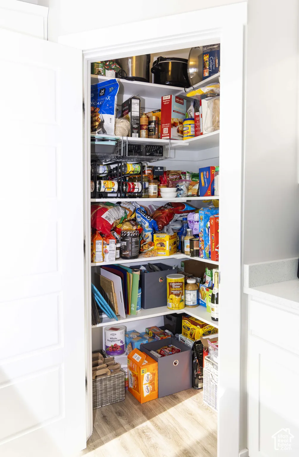 Walk-in pantry featuring white painted shelving, corner storage configuration, and wood-finish flooring