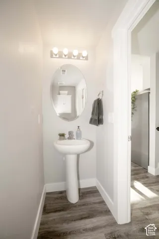 Pedestal sink with chrome faucet, oval wall-mounted mirror, four-light vanity fixture, and LVP flooring