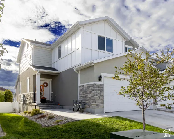 Two-story exterior featuring a mix of horizontal siding, vertical board-and-batten siding, and stone veneer accents, complete with a concrete driveway and attached garage