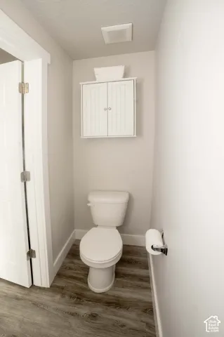 Neutral-toned space featuring LVP flooring, a white porcelain toilet, wall-mounted white shaker-style cabinetry, and polished chrome hardware