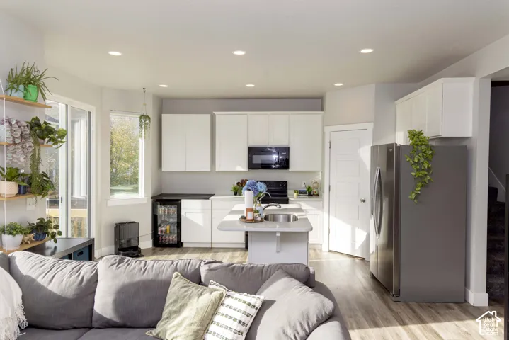 Kitchen featuring white cabinetry, integrated stainless appliances, a center island with a built-in sink, LVP flooring, and recessed lighting