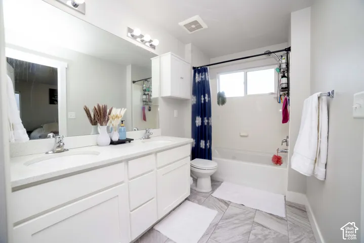 Bathroom featuring dual-sink vanity with light-toned countertop, wall-to-wall mirror, built-in cabinetry, tub-shower combination with surround, and tile flooring