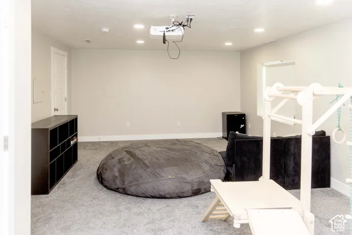 Neutral-toned interior featuring wall-to-wall carpeting, recessed LED lighting, a ceiling-mounted projector, and a single-panel interior door