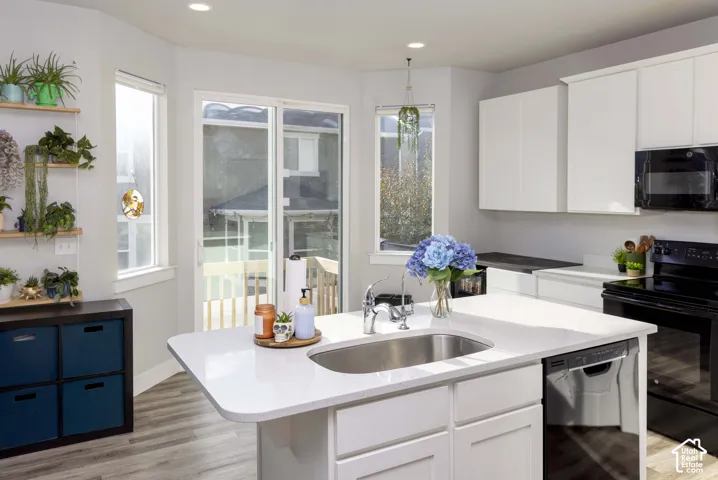 Kitchen featuring a central island with a quartz countertop and integrated stainless steel sink, white cabinetry, LVP flooring, and sliding glass doors
