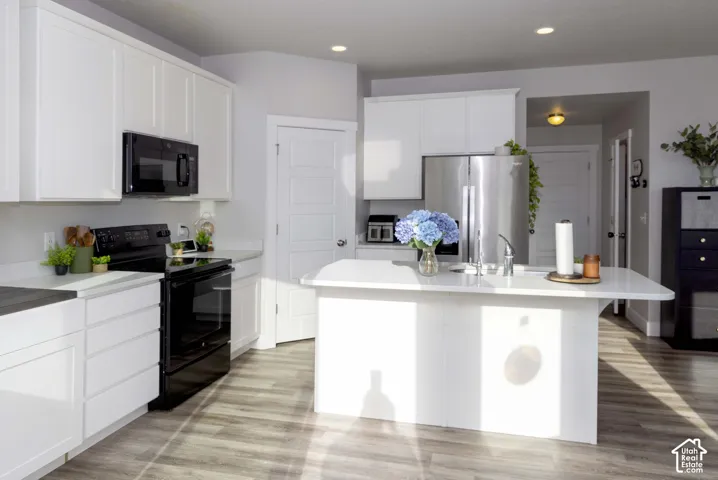 Kitchen featuring white shaker-style cabinetry, quartz countertops, a central island with an integrated sink, stainless steel appliances, and LVP flooring