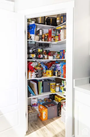Walk-in pantry featuring white painted shelving, corner storage configuration, and wood-finish flooring