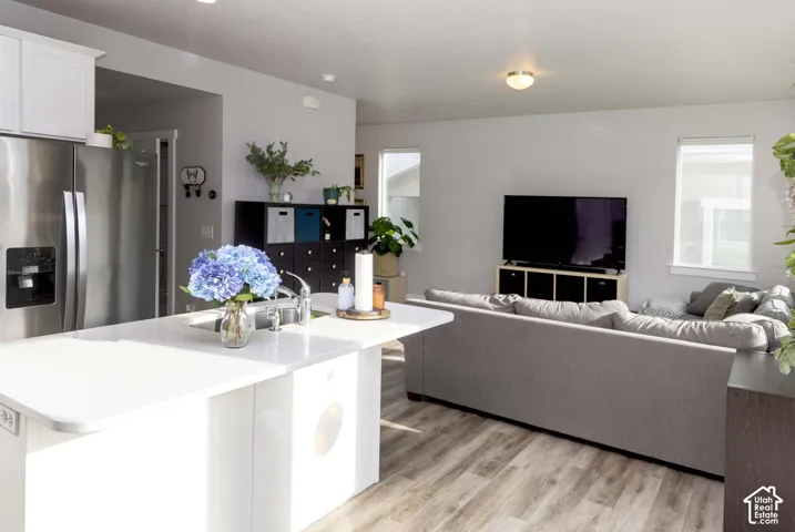 Kitchen featuring an island with a quartz countertop, stainless refrigerator, white cabinetry, and LVP flooring