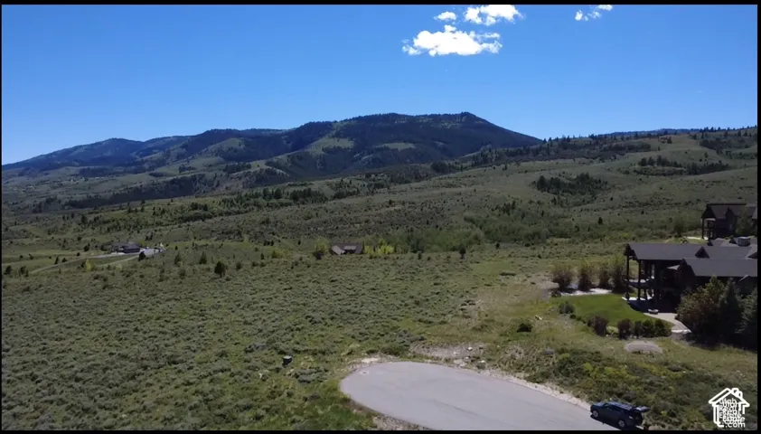 Aerial perspective featuring mountain landscape, native vegetation, asphalt cul-de-sac, and multi-level residence with dark shingled roofing
