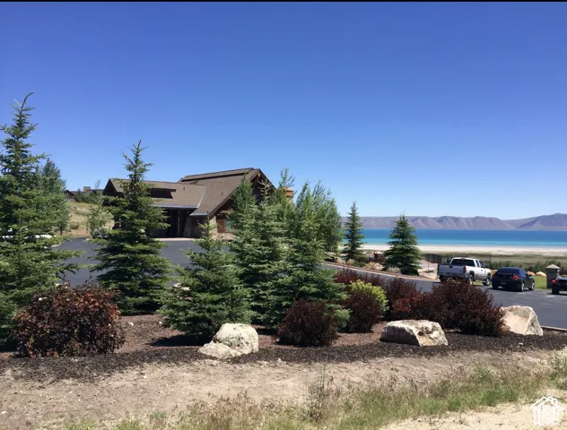 Wood-sided residence featuring a multi-pitched roof, paved driveway, mature coniferous landscaping, and water frontage