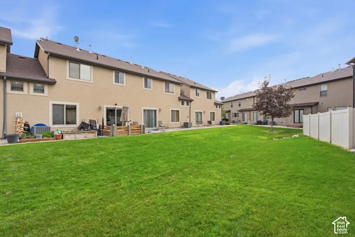 Expansive backyard featuring a large grass lawn, perimeter vinyl fencing, and multiple sliding glass door entries