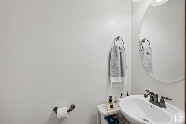 Oval wall-mounted mirror, white pedestal sink, oil-rubbed bronze double-handle faucet, and matching oil-rubbed bronze towel ring and toilet paper holder