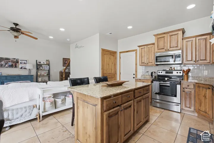 Kitchen featuring stained wood cabinetry, a central island with a stone-composite countertop, tile flooring, stainless steel appliances, and recessed lighting