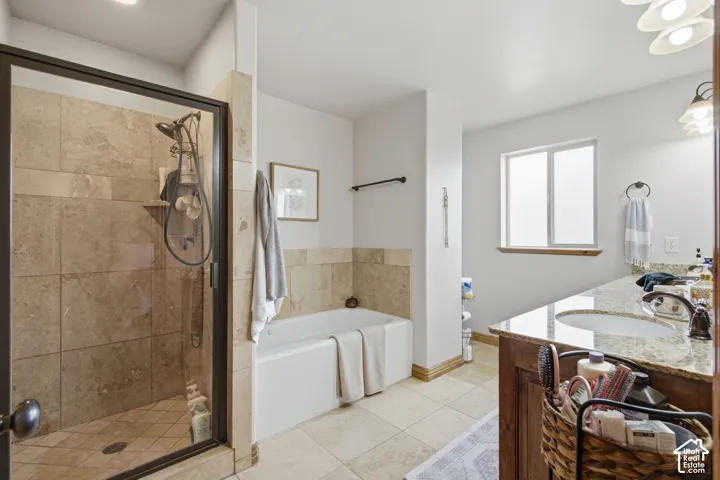 Bathroom featuring a walk-in shower with stone tile surround, a built-in soaking tub, stone tile flooring, a stone-topped vanity with an undermount sink, and dark wood-finish cabinetry