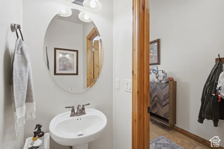 Oval wall-mounted mirror with integrated three-bulb vanity lighting, ceramic pedestal sink, and metallic faucet hardware