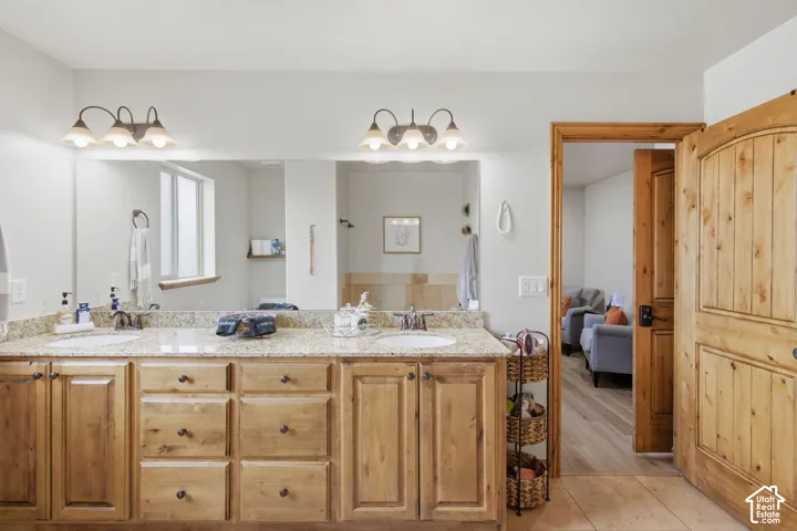 Double vanity with stone countertop, dual undermount sinks, custom wood cabinetry, and dual wall-mounted light fixtures