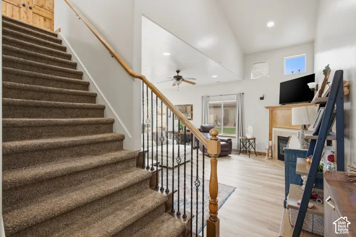 Staircase featuring a wood handrail with metal balusters, high ceilings, wood-finish flooring, and a fireplace with a wood mantel