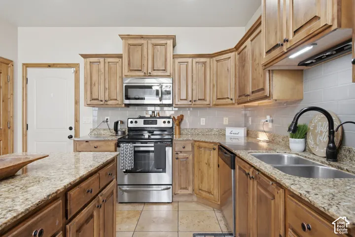 Kitchen featuring stained wood cabinetry, stone-surface countertops, subway tile backsplash, stainless steel appliances, and a central island