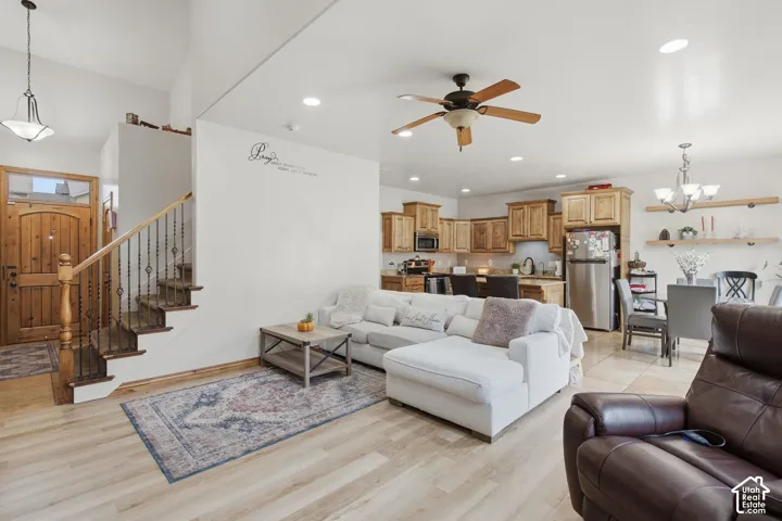 Open-concept floor plan featuring high ceilings, wood-finish flooring, a staircase with decorative metal balusters, kitchen cabinetry with integrated stainless steel appliances, and wall-mounted floating wood shelving