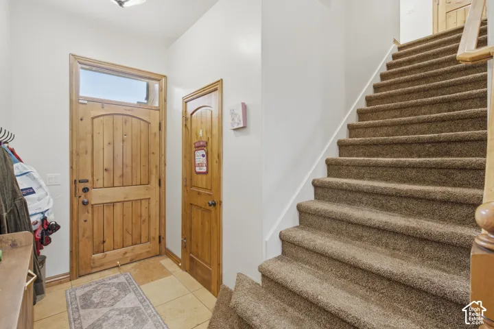 Entryway featuring a natural wood-finish door with an overhead transom window, tile flooring, and a carpeted staircase with a wooden handrail