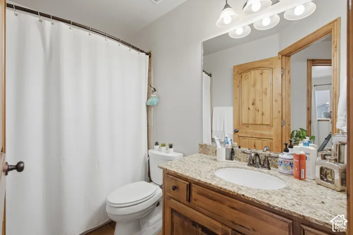 Bathroom featuring a vanity with stone-patterned countertop, under-mount sink, multi-light fixture, wood cabinetry, and solid wood-trim interior door