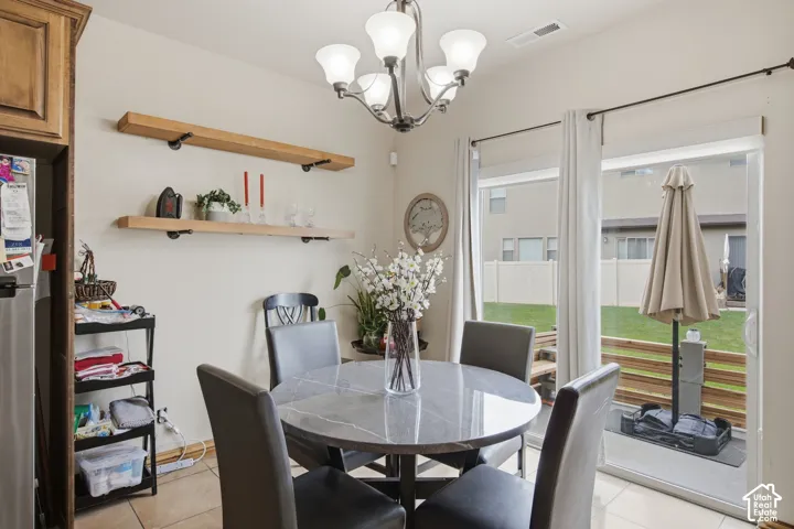 Dining area featuring a brushed-nickel chandelier, natural wood-finish floating shelving with industrial-style brackets, sliding glass patio doors, and tile flooring