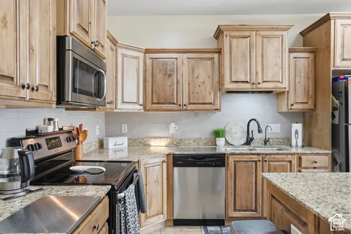 Kitchen featuring medium-tone wood cabinetry, natural stone countertops, subway tile backsplash, stainless steel appliances, and a high-arch pull-down faucet