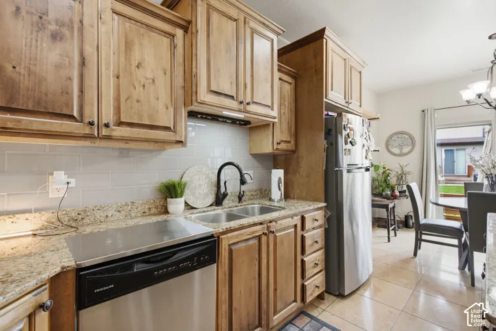 Kitchen featuring stained wood cabinetry, stone-surface countertops, subway tile backsplash, stainless steel appliances, and tile flooring