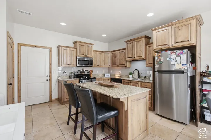 Kitchen featuring stained wood cabinetry, stone countertops, central island, stainless steel appliances, and ceramic tile flooring