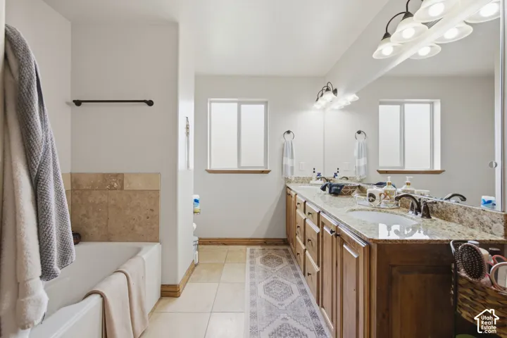 Dual-sink vanity with stone countertop, wood cabinetry, large wall-mounted mirror, and tile-surround bathtub